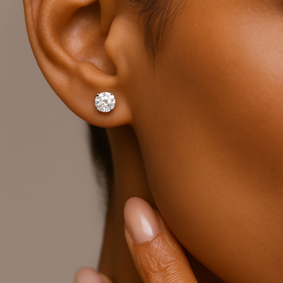 Close-up of a woman wearing a round diamond stud earring, with her hand gently touching her jawline.